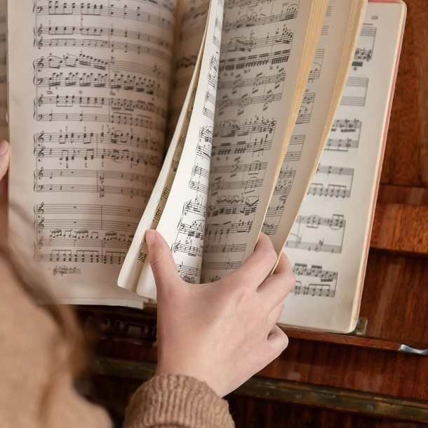 A woman pianist sits at the piano leafing through the notes.